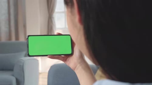 Female Using A Smartphone With Green Screen Mock Up Display At Home Living Room