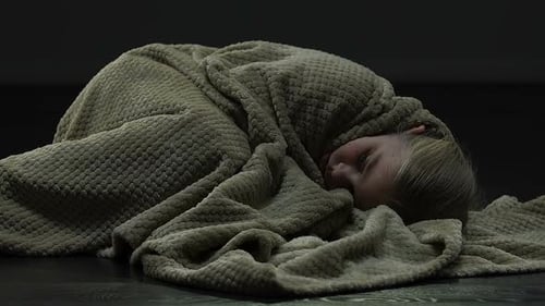 Fille effrayée bronchant de peur, allongée sur le sol et couvrant la tête avec une couverture