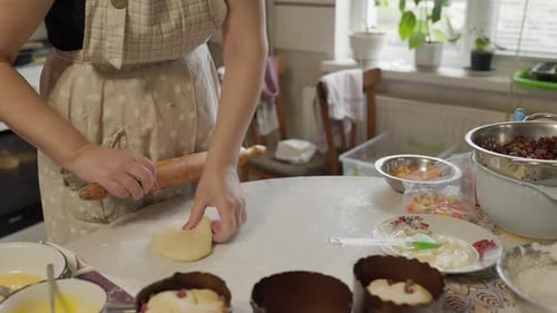 Women rolling out Dough on table top with flour dusted on so it does not stick with wooden rolling