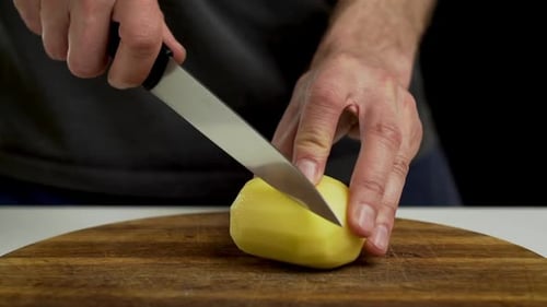 Chef coupant et tranchant la pomme de terre pelée sur une planche à découper, gros plan