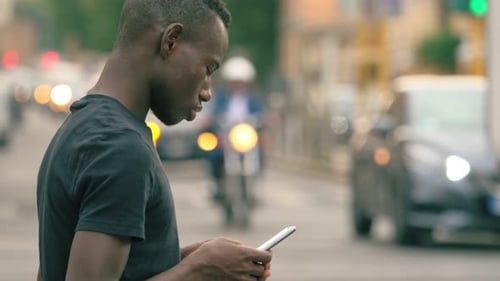young african man types on smartphone in the street