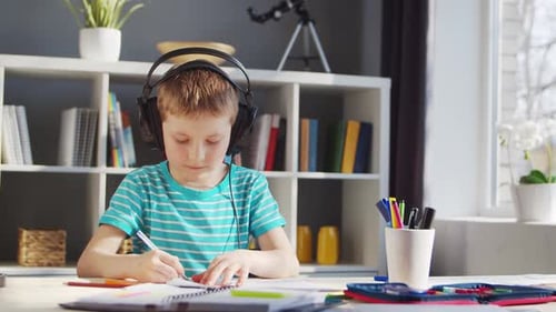 Boy Writes in Notebook Wearing Headphones Indoors