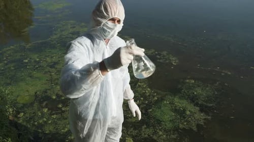 Scientist Holds Water Sample in Beaker by Algae Filled Water