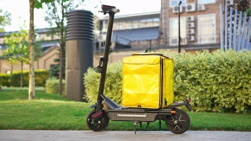 Escooter panorámico con vista lateral sobre el pavimento con mochila amarilla para entrega de alimentos