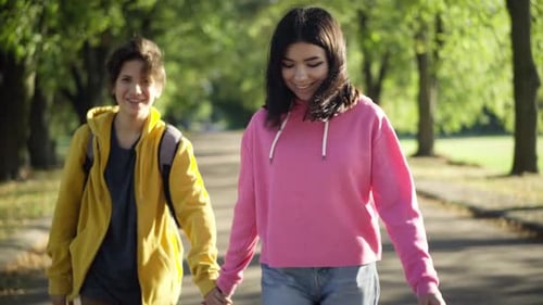 Happy Teenage Couple Holding Hands Walking in Sunrays in Summer Park Smiling