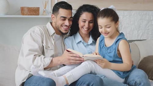 Hispanic Family Sitting on Couch at Home on Weekend Reading Book Together