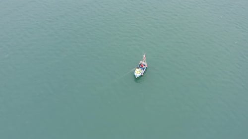 Fischerboot zieht an einem grauen Tag Netze aus der Luft