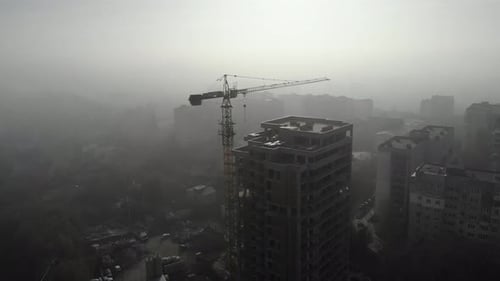 Birds eye view on tower crane in fog standing next to residential building.