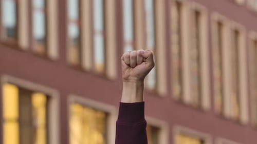 Raised Male Hand with Clenched Fist for Protest Against the Background of the City Street. Cropped