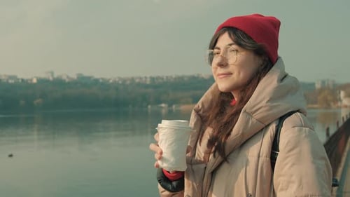 Young girl with glasses looks at the sun and drinking coffee