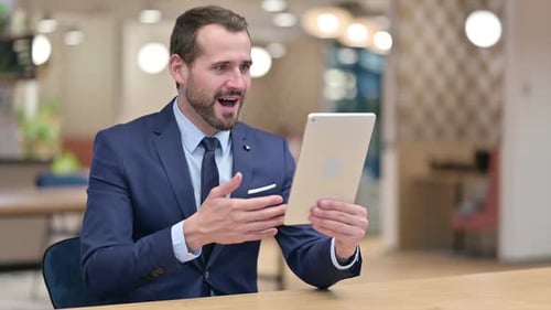 Man Celebrates Success While Using Tablet at Desk