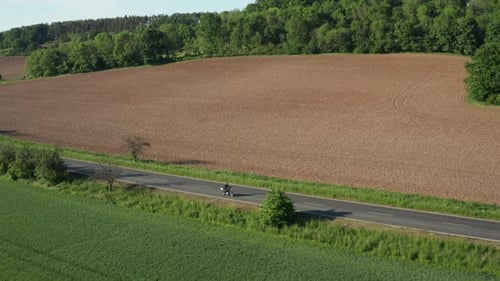 Motorbiker Rides on Empty Road Past Yellow Field at Sunset