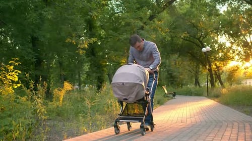 Papai de jeans e camisa xadrez caminha pelo parque com um carrinho de criança e ajusta a criança. Um homem