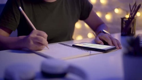 Weibliche Hände schreiben in ein Notizbuch und benutzen nachts das Smartphone