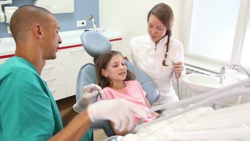 Girl sitting in the dental chair giving high five to dentist and assistant