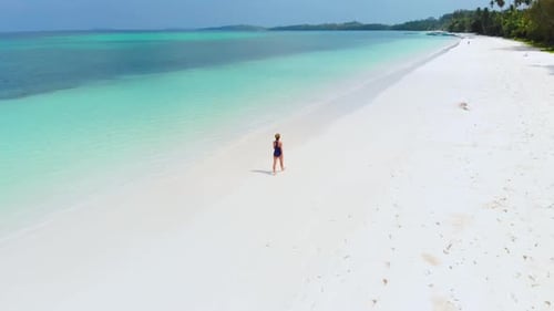 Aerial: Woman walking on white sand beach turquoise water tropical coastline Pas
