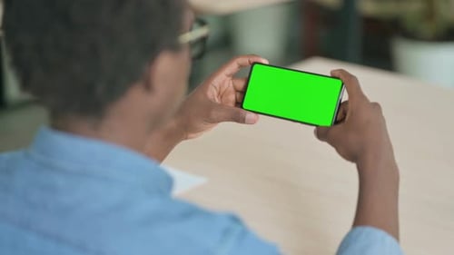Man Holds Phone With Green Screen at Desk