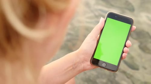 NICE, FRANCE - JULY 2017 Female on the beach with green screen display phone