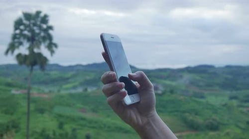 Hand Holds Smartphone on Green Hillside