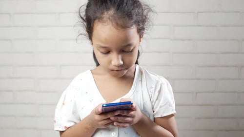 Girl Using Smartphone in Front of Brick Wall