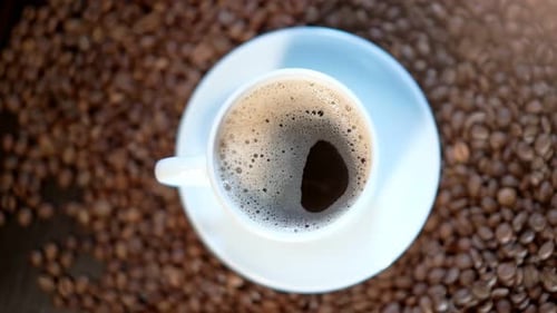 A Closeup of a White Cup Filled with Tasty Aromatic Coffee Among Coffee Beans