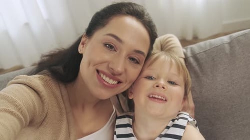Smiling Mother and Child Cuddle on Couch Indoors