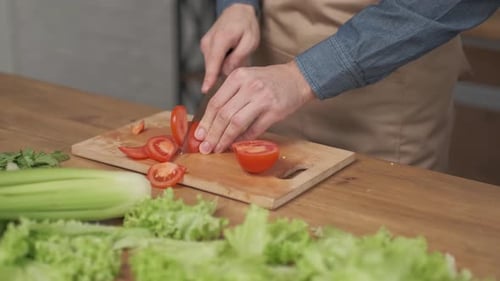 }Close up shot of man hands slicing vegetables on wooden cutting board for salad on the table