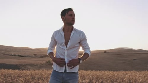 Homem desabotoa camisa no meio do campo de trigo em um dia quente de verão