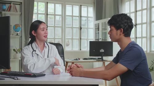 Asian Woman Doctor Is Talking With Young Male Patient During Consultation In A Health Clinic
