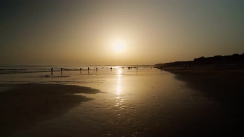 Silhouette von Menschen, die bei Ebbe bei Sonnenuntergang Touristen am Strand vor dem Hintergrund der