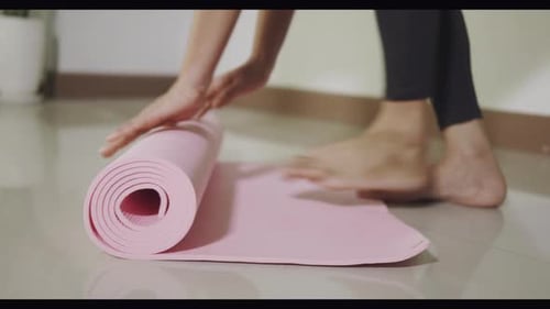 Woman rolling pink yoga mat before or after sport preparation working out