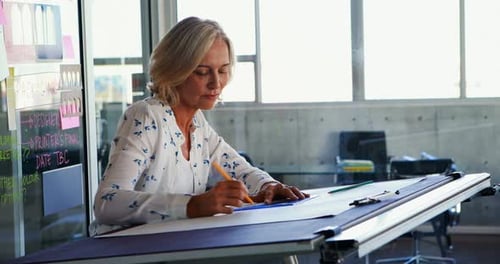 Female architect working on blueprint over drafting table