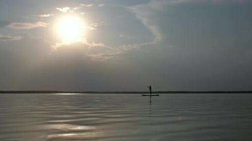 Silhouette of Young Female Paddle Boarding at Sunset