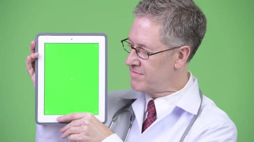 Mature Doctor Holding Tablet with Green Screen