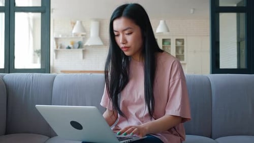 Woman works on laptop sitting on couch at home