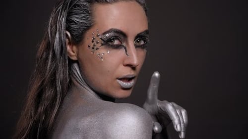 Portrait of a Young Woman with Silver Paint on Her Skin and Hair in the Studio
