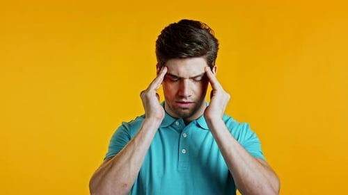 Young Man Having Headache, Studio Portrait. Guy Putting Hands on Head, Isolated on Yellow Background