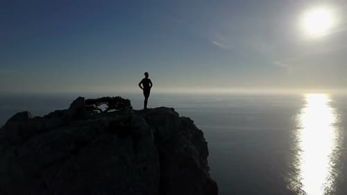 Aerial Silhouette of Young Woman Standing on the Top of a Mountain Facing the Sea