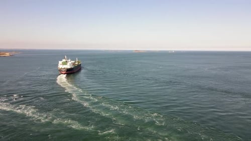 Aerial shot of a fuel tanker leaving harbor, with tugboat manoeuvring away. Drone dolly left