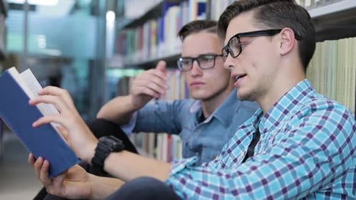 Students Reading Book At College Library Near Bookshelves