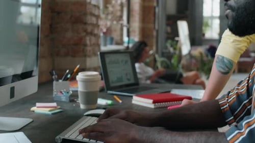 Homme afro utilisant un ordinateur et parlant avec un collègue caucasien au travail