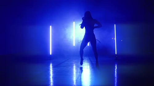 Frau im sexy Outfit mit Absätzen tanzt sinnlich im dunklen Studio mit blauen Lampen