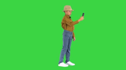 Little Boy in a Straw Hat Showing Around While Having Video Call on the Phone on a Green Screen