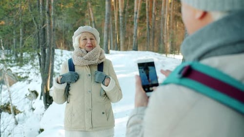 Happy Elderly Lady Tourist Posing for Smartphone Camera in Snowy Park in Winter