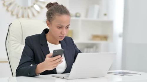 African Businesswoman Using Smartphone and Laptop in Office
