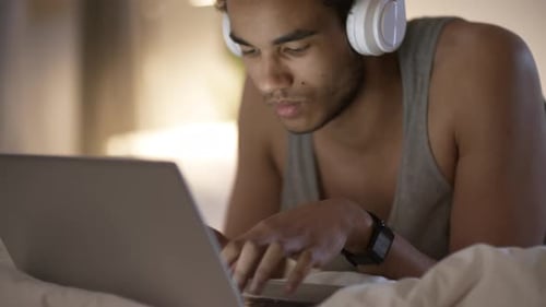 Young Adult Types on Laptop in Bed with Headphones