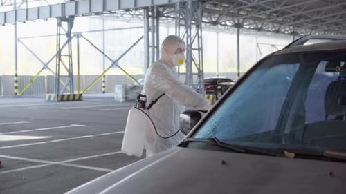 Worker Disinfecting Car in Protective Suit and Mask