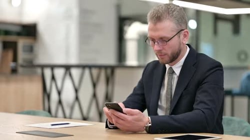 Attractive Young Businessman Using Smartphone in Office
