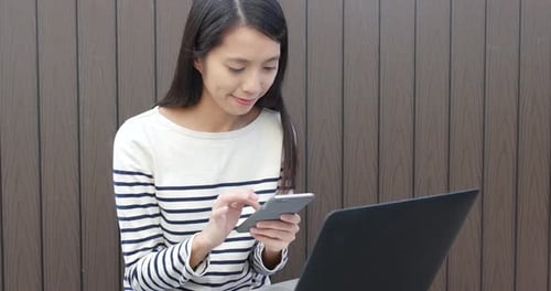Young Woman Uses Smartphone Next to Laptop