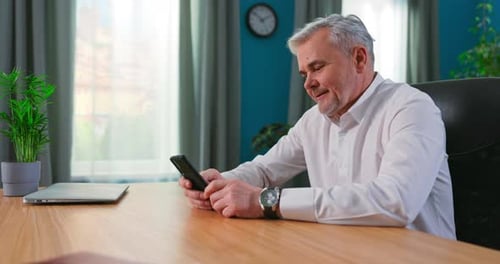 Man Using Mobile Phone at Wooden Desk Indoors